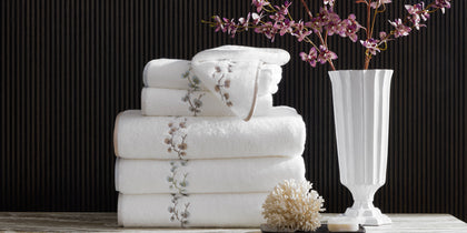 White Jasmine Giza towels with an embroidered floral vine, stacked beside a coral decoration and a vase of orchids.