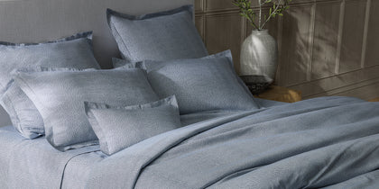 Blue-gray Jasper pebbled print bedding styled on a bed with a paneled headboard.
