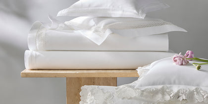 White Lace Pique sheets stacked on stone tables, with a floral lace-trimmed sham.