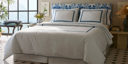 White Louise bedding with blue bordered trim, styled on a bed with a floral headboard.