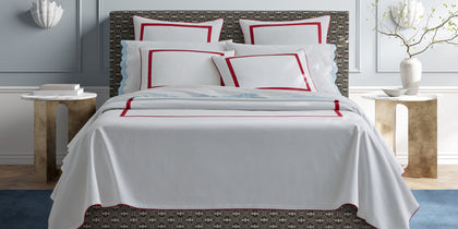 White Louise Pique bedding with red bordered trim, styled on a patterned bed frame.