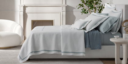 White Lowell Matelasse quilted bedding with sage trim, styled on a bed near a potted plant.