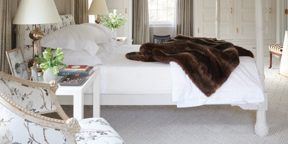 White Luca Hemstitch bedding styled on a bed with a brown faux fur throw.