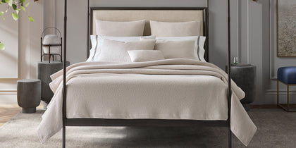 Ivory Malibu textured bouclé bedding styled on a bed with a dark four-poster frame.