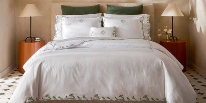 White Marcella bedding with green vine-embroidered scalloped border, styled on a bed.