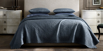 Slate blue Margaret textured quilted bedding, styled on a bed with a tan upholstered headboard.