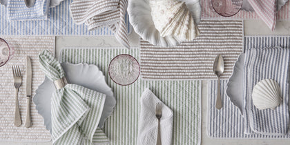 Multicolor striped Matteo placemats and napkins arranged with scalloped plates and seashells.