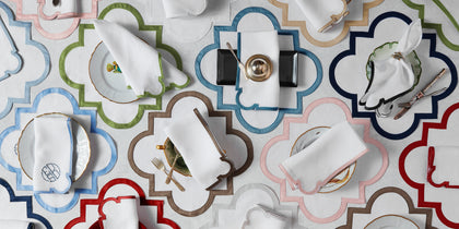 Scalloped Mirasol placemats in assorted colors arranged in a grid with napkins and place settings.