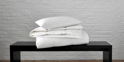 Montreux white down pillow and comforter stacked on a black bench