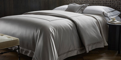 Silver-gray Nocturne sateen bedding styled on a bed with a tufted bench and patterned headboard.