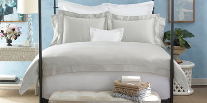 White and gray Nocturne Hemstitch bedding styled on a bed in a blue-walled bedroom.