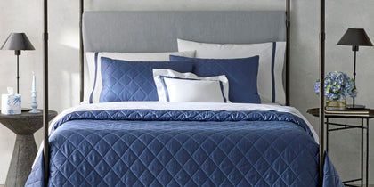 Navy diamond-quilted Nocturne Quilt bedding on a four-poster bed with lit candles and hydrangeas.