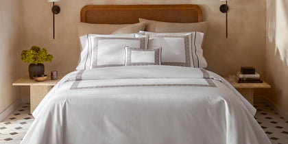 White Ophelia Pique bedding with taupe Greek key trim on a bed with a rattan headboard.