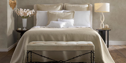 Textured cream Perla bedding styled on a bed with a tufted bench and fresh flowers.