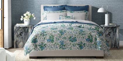 White and green Pomegranate floral-print bedding styled on a bed between marble side tables.