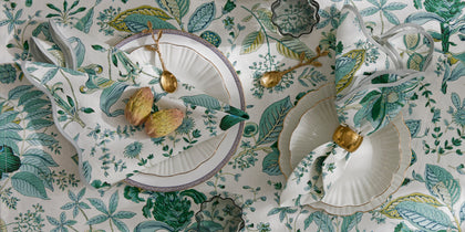 Green leaf-print Pomegranate tablecloth and napkins set with white china and gold accents.