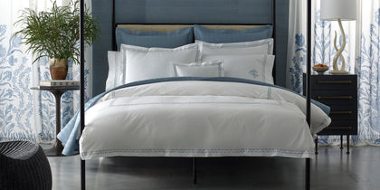 White Prado bedding with blue zigzag trim on a four-poster bed with blue floral curtains.
