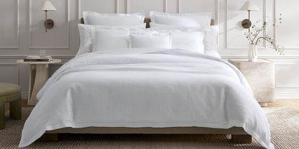 White linen Roman Hemstitch bedding styled on a bed in a paneled bedroom.