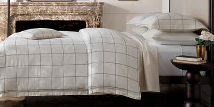 Sebastian white windowpane-embroidered bedding styled on a bed by a fireplace