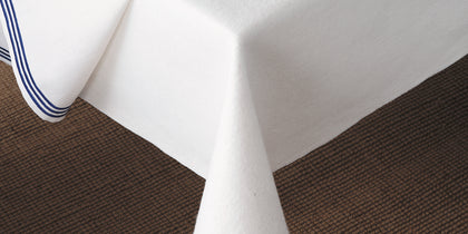 White table silencer padding with blue striped trim draping over a table edge onto a woven rug.