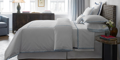 White Stella bedding with blue scalloped trim on a bed near a fretwork console.