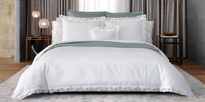 White Virginia bedding with floral lace trim styled on a bed with a sage green throw.
