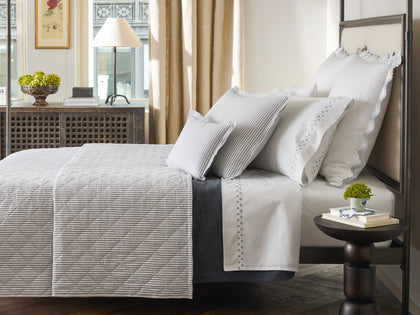 Gray diamond-quilted Matteo coverlet styled on a four-poster metal bed in a sunlit bedroom.