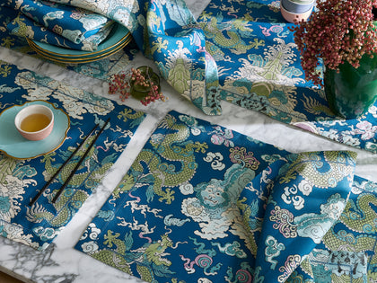 Blue Magic Mountain dragon print placemats and napkins set with teacups, chopsticks, and pink berries.