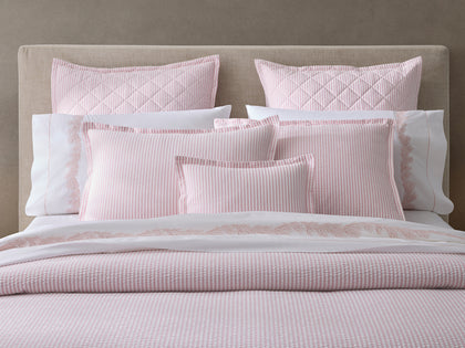 Pink-striped Matteo bedding with quilted shams and embroidered leaf-trim sheets, styled on an upholstered bed.