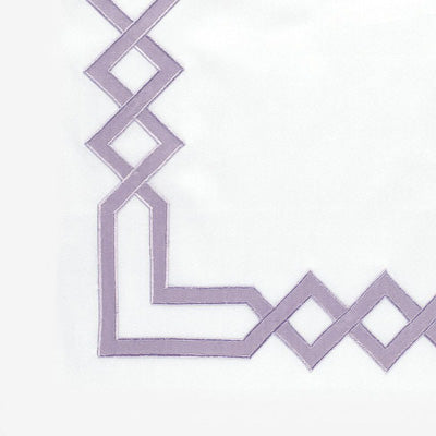 A close-up of a white napkin featuring a lavender embroidered geometric corner pattern.