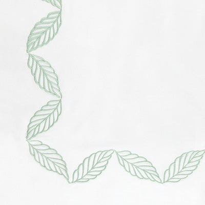 Close up of a napkin featuring a light green embroidered leaf border along the left and bottom edges.